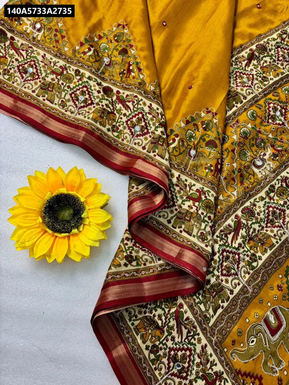 TRENDBUY Mustard Yellow Mulmul Cotton Saree with Cream Patola Print and Aari work pallu, flat lay with sunflower