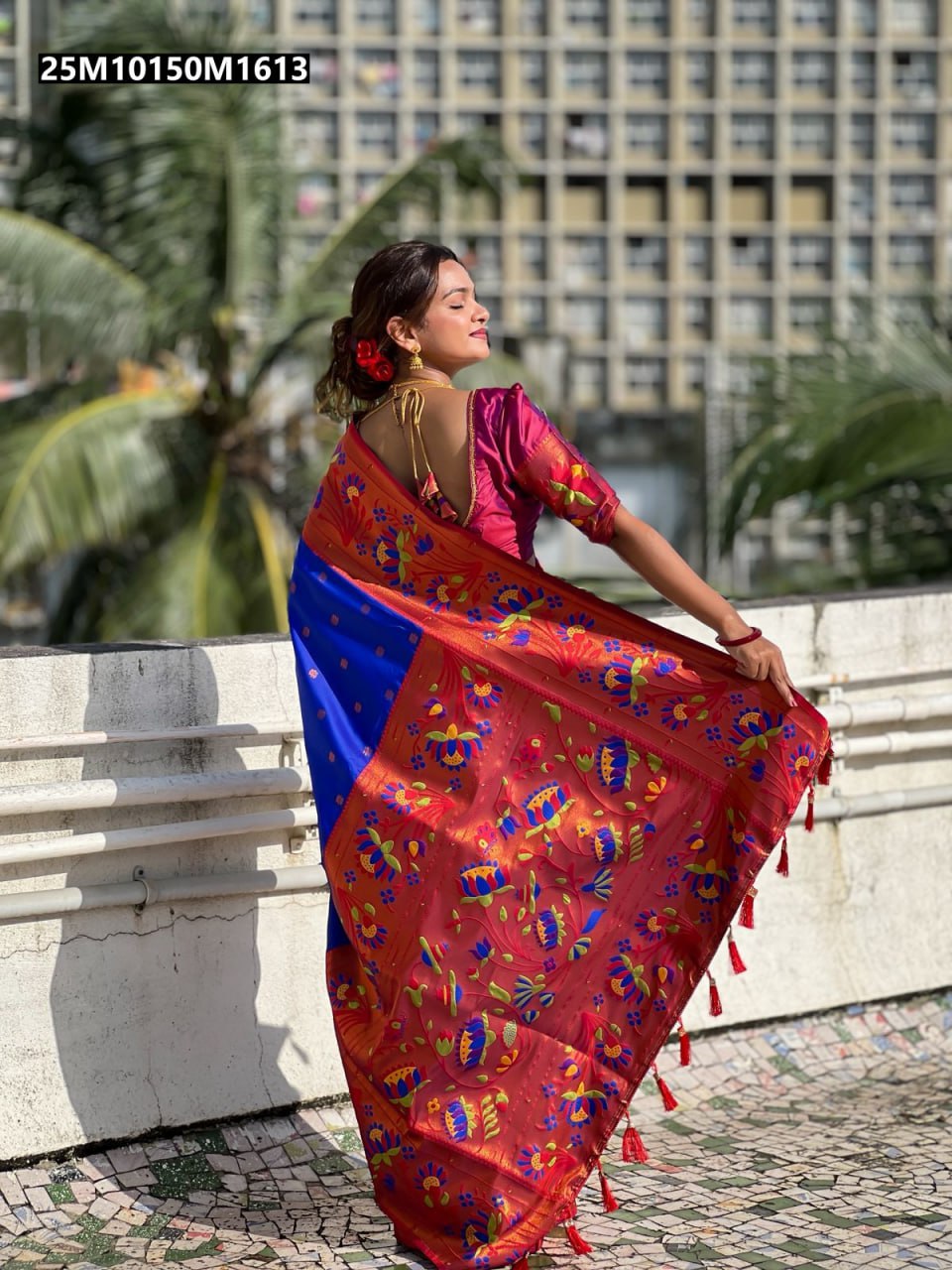 Woman in a royal blue and red soft silk saree with intricate zari and meenakari designs, standing outdoors.