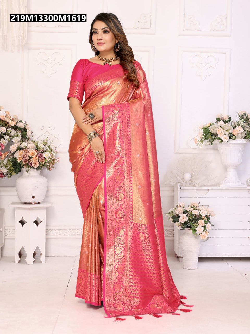 A woman elegantly posing in a radiant Rani Pink and Gold Weave Banarasi Tissue Silk Saree, featuring intricate butti work and a rich contrast pallu, in a luxurious white room setting.
