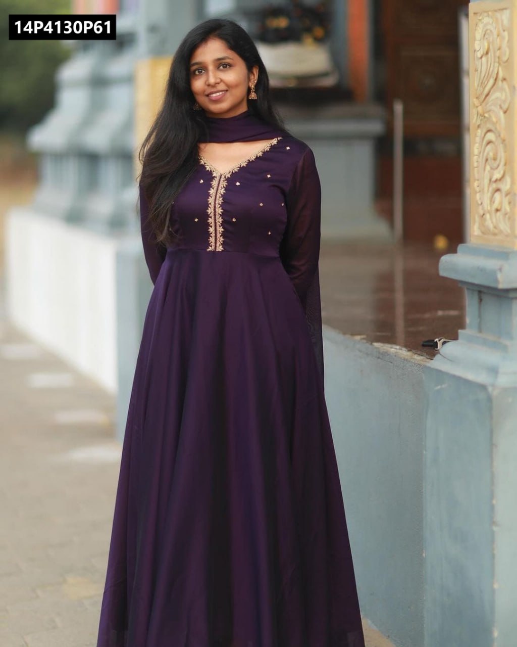 Full body shot of a model standing elegantly in a deep purple embroidered Faux Georgette Anarkali kurti and Georgette dupatta, against an architectural background.