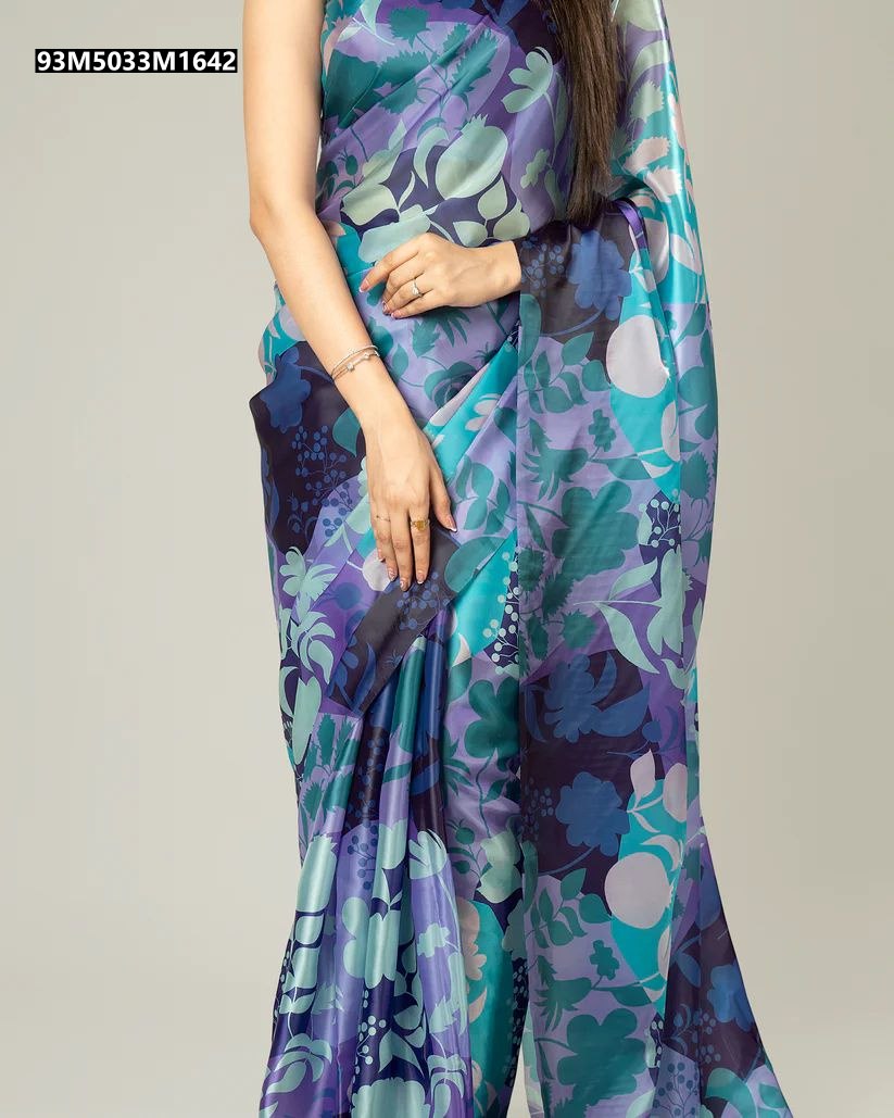 Close-up of a woman's midsection and arm, showing the intricate teal blue, lavender, and deep purple floral print on a shiny Japan satin saree, against a neutral background.