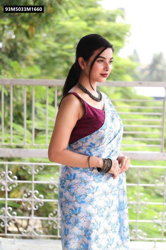 Model in a light blue and white Japan satin printed saree with blue floral motifs, paired with a maroon blouse, standing outdoors.