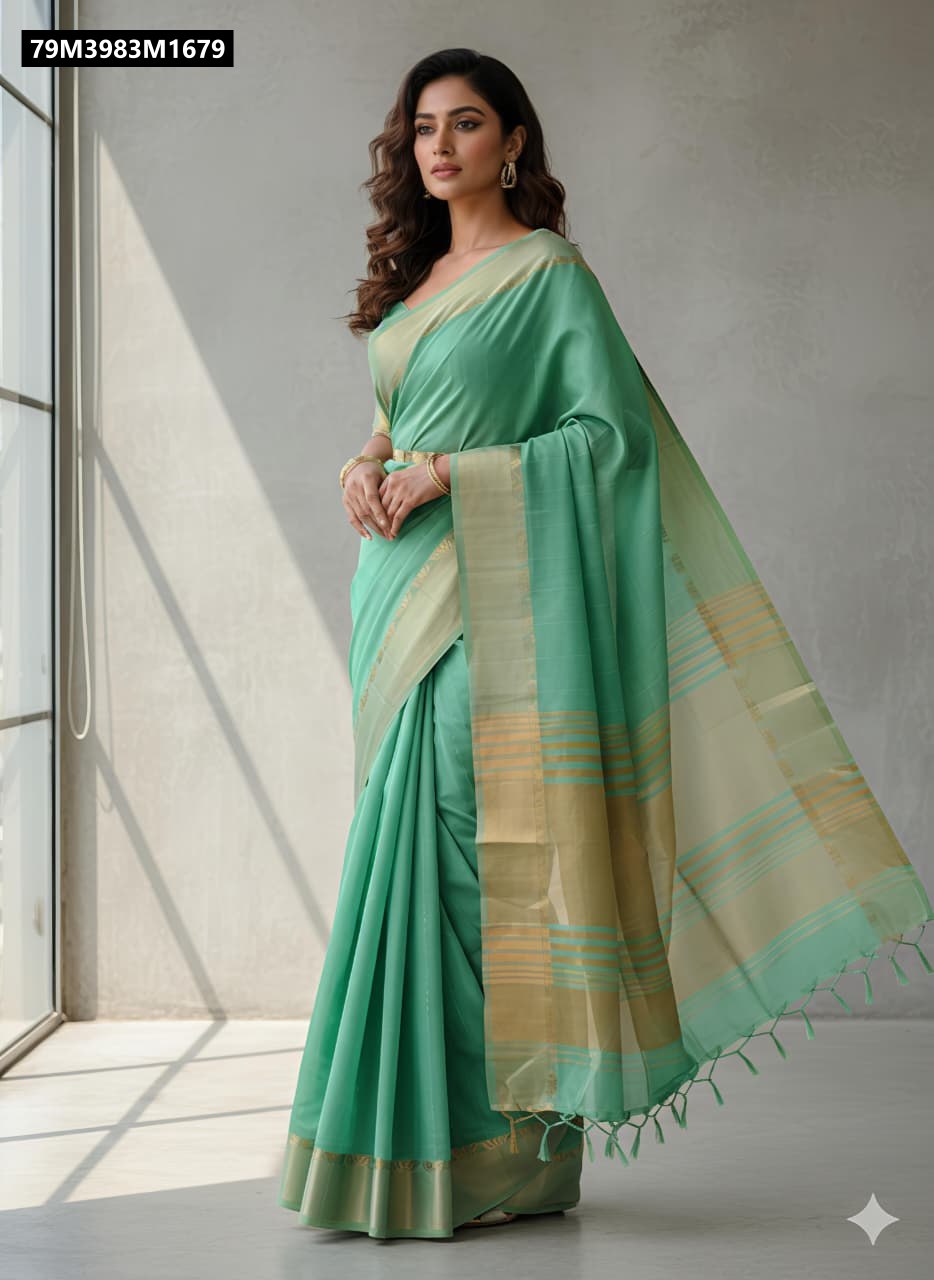 A woman elegantly draped in a mint green Tani Bani silk saree with a gold jacquard border, posing by a sunlit window.