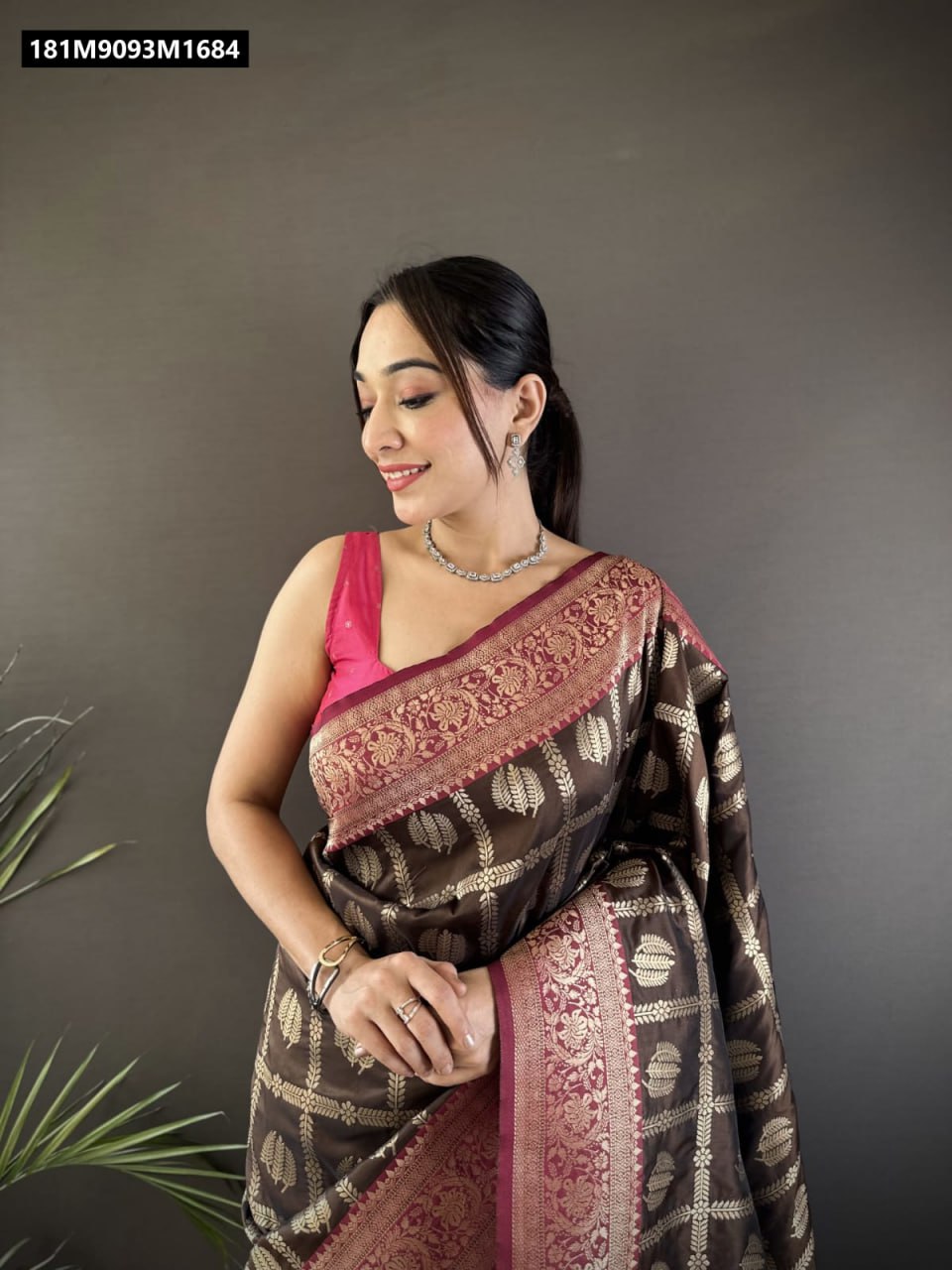 Model smiling, posing in a coffee brown Banarasi Lichi silk saree with gold zari weaving and a maroon border and pallu, featuring a bright pink sleeveless blouse.