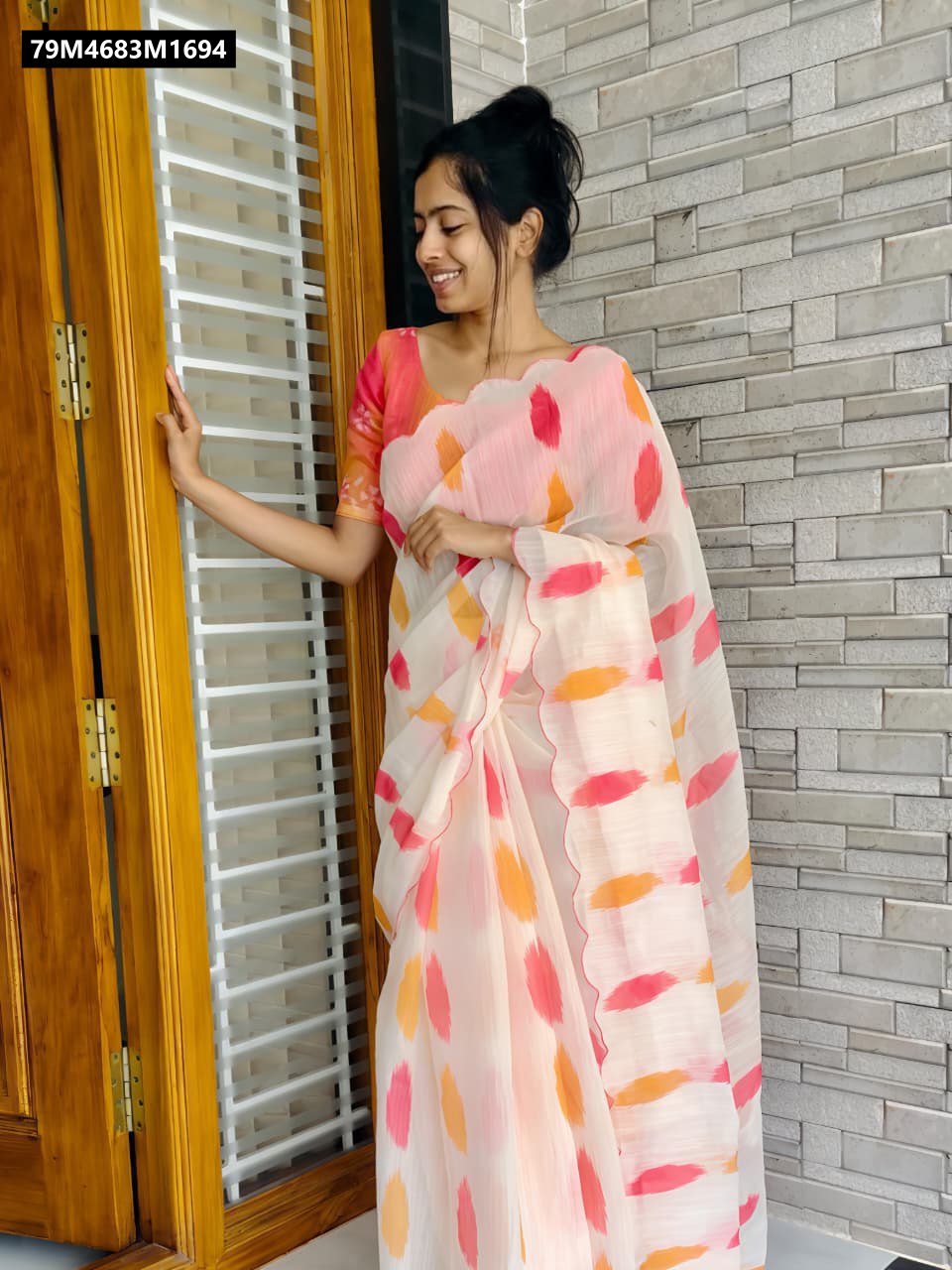 A young woman gracefully modeling the TRENDBUY multi-color digital print linen saree, showcasing its elegant drape and vibrant patterns, standing by a wooden door against a brick wall.