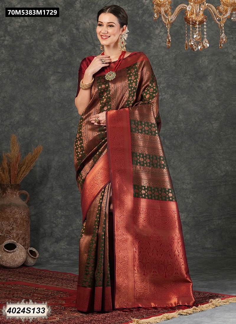 A smiling woman elegantly poses in a rich olive green Kanjivaram silk saree with intricate maroon and gold zari weaving, featuring a broad maroon border and pallu, standing on an ornate rug.