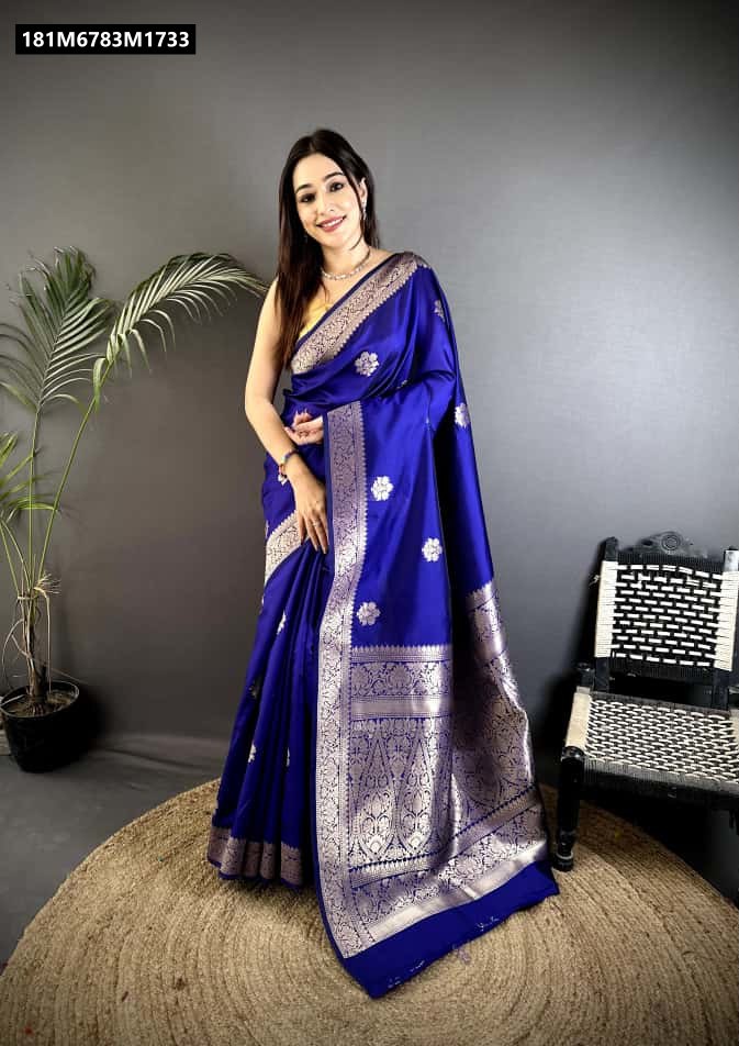 Model showcasing a Royal Blue Banarasi Cotton Silk Saree with gold Zari weaving, draped elegantly, standing next to a plant and woven chair.