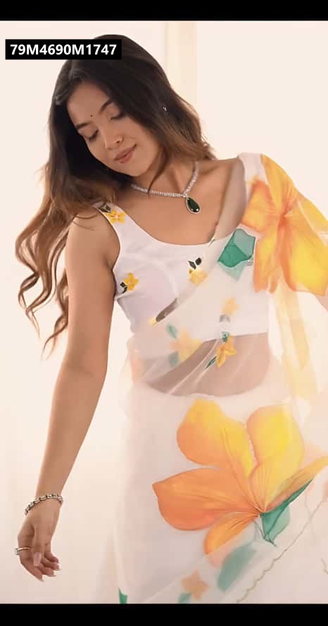 Mid-shot of a smiling model wearing the TRENDBUY white paper georgette saree with orange and yellow floral print, showcasing the matched sleeveless blouse and a delicate necklace.