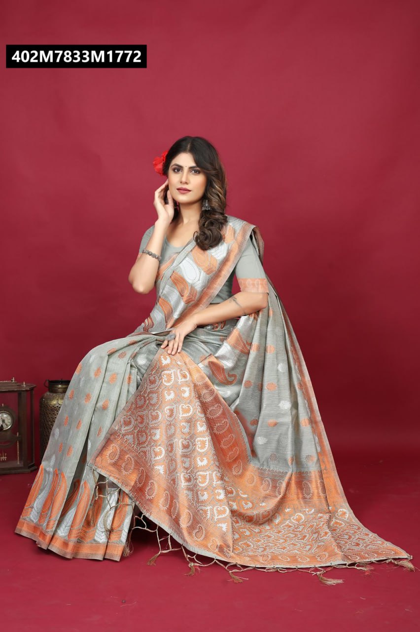 A woman gracefully seated, wearing a light grey Pure Linen Silk saree with intricate orange and silver weaving patterns, holding a red flower in her hair.