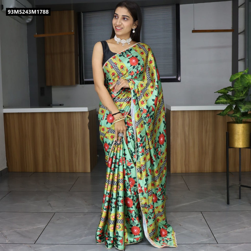 A smiling woman elegantly poses in a mint green and golden yellow floral printed satin saree with red flowers and a delicate pearl lace border, paired with a black sleeveless blouse, looking confident and poised.