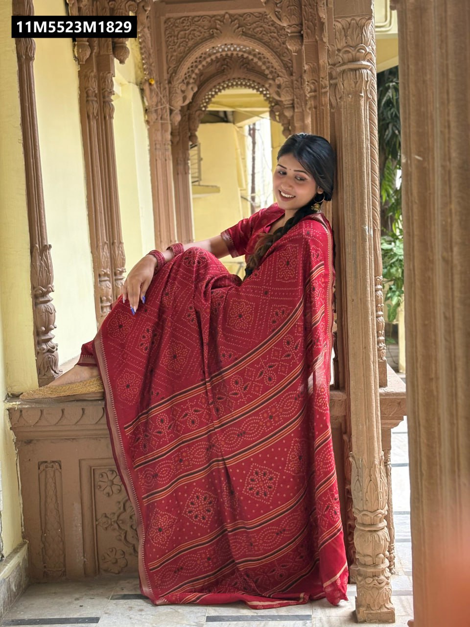 Stylish woman in a Red TRENDBUY Mangalagiri Silk Saree with Bandhani print, sitting and smiling, showcasing the saree's drape and design in a traditional setting.