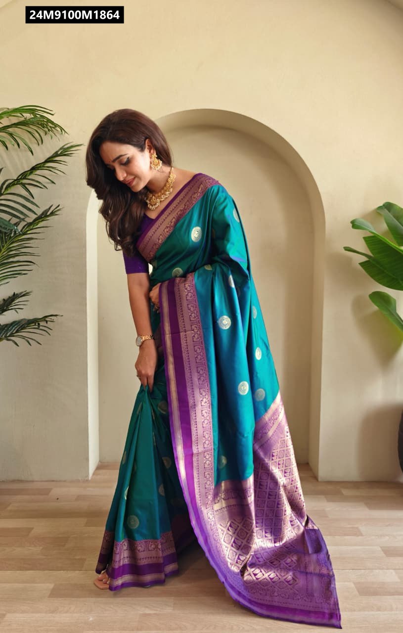 Model gracefully posing in a vibrant Aqua Blue and Royal Purple soft silk saree, featuring gold coin weaving and an intricate contrast border and pallu, standing next to potted plants.