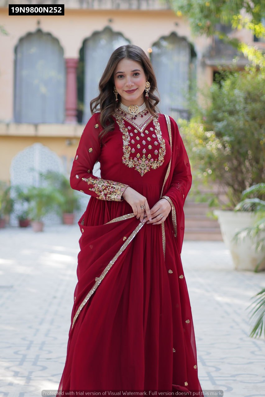 Front full body view of a smiling model wearing a maroon TRENDBUY Faux Blooming Georgette gown, highlighting the sequin embroidered V-neck bodice and long sleeves, against a soft outdoor backdrop.