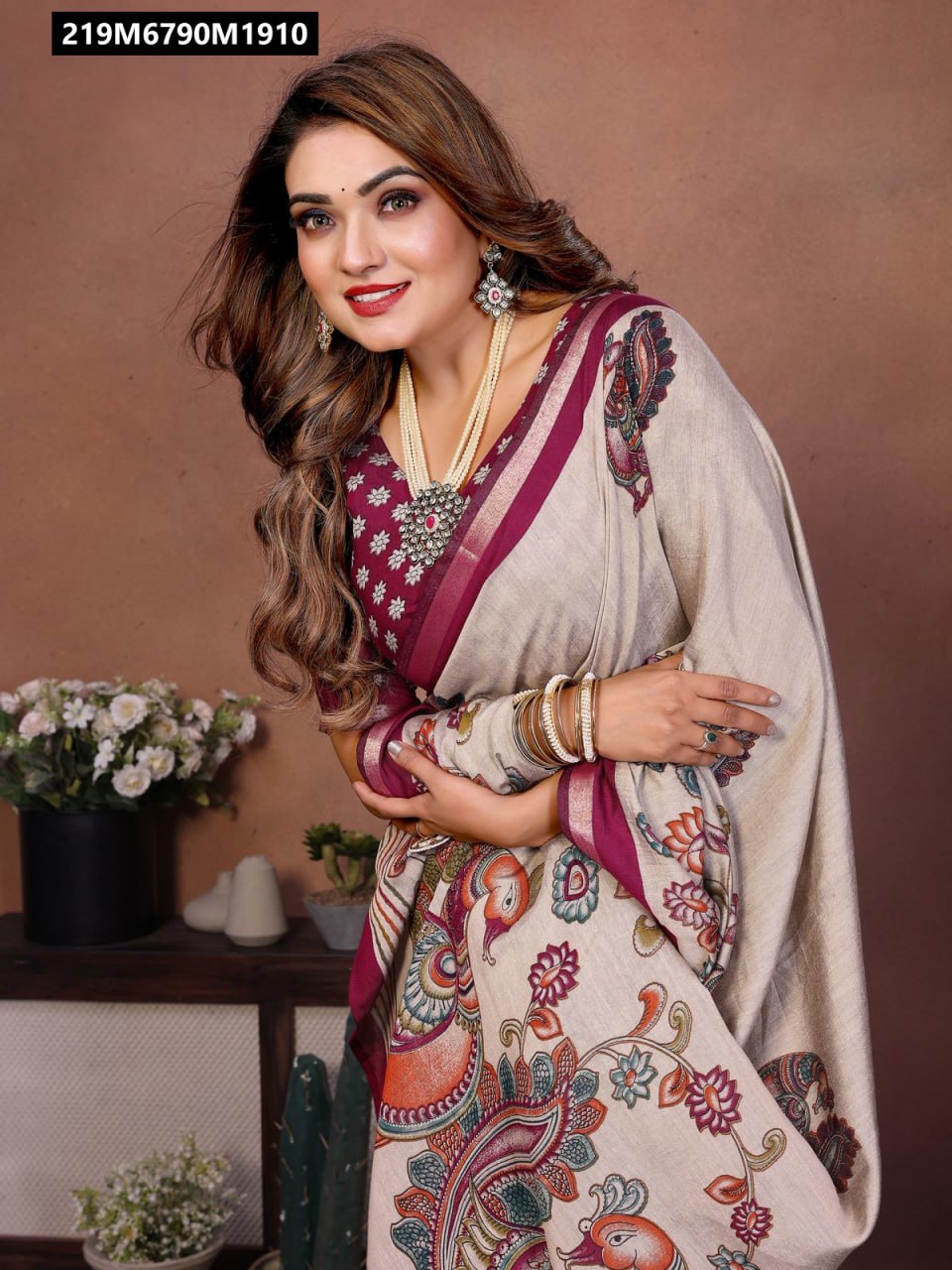 Close-up of a smiling woman in a cream mul cotton saree with maroon border and intricate Kalamkari bird and floral prints, accessorized with pearls.