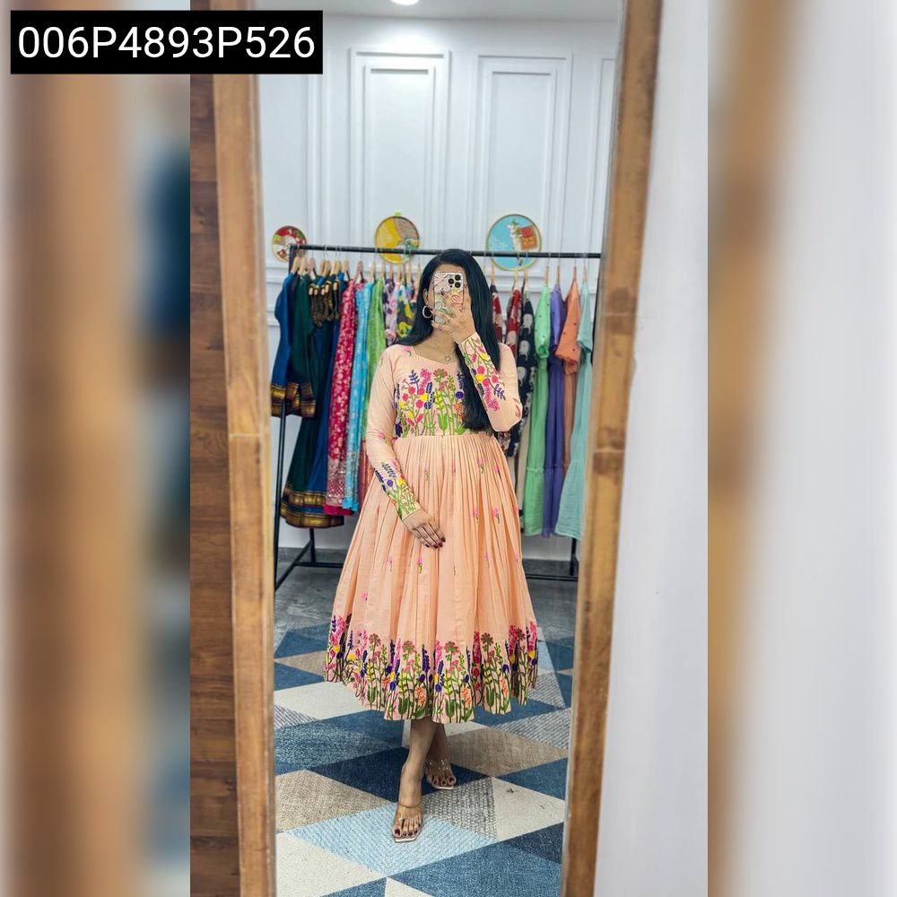 Full body shot of a model wearing the TRENDBUY peach Maska cotton maxi dress with multi-color floral embroidery, reflected in a mirror against a background of various apparel. The dress flows gracefully, highlighting its length and fit.