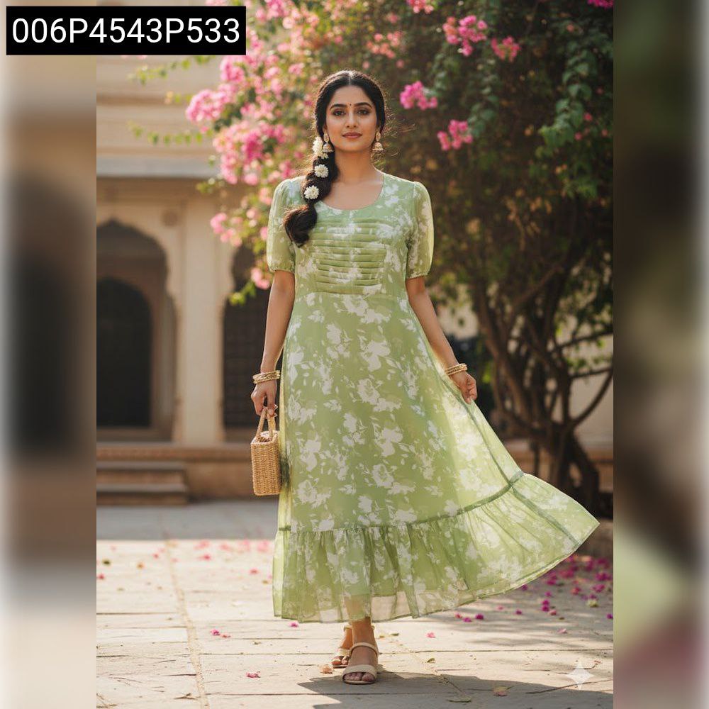 Elegant woman in sage green floral maxi dress with straw bag, posing amidst blooming pink flowers.