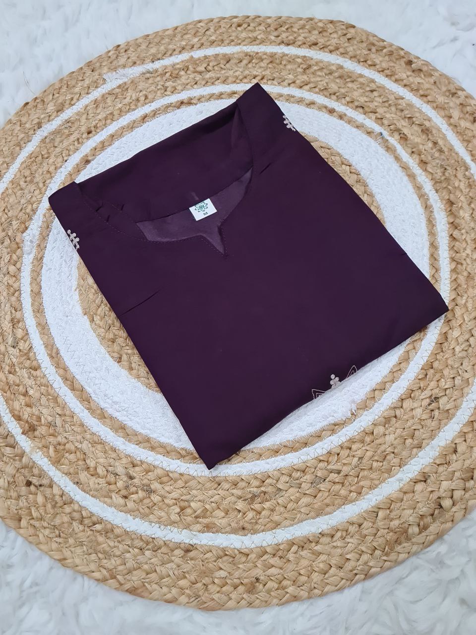 Folded TRENDBUY ST-SWATI wine PV Chanderi kurti, showcasing the front neck design and subtle embroidery, placed on a round jute mat.