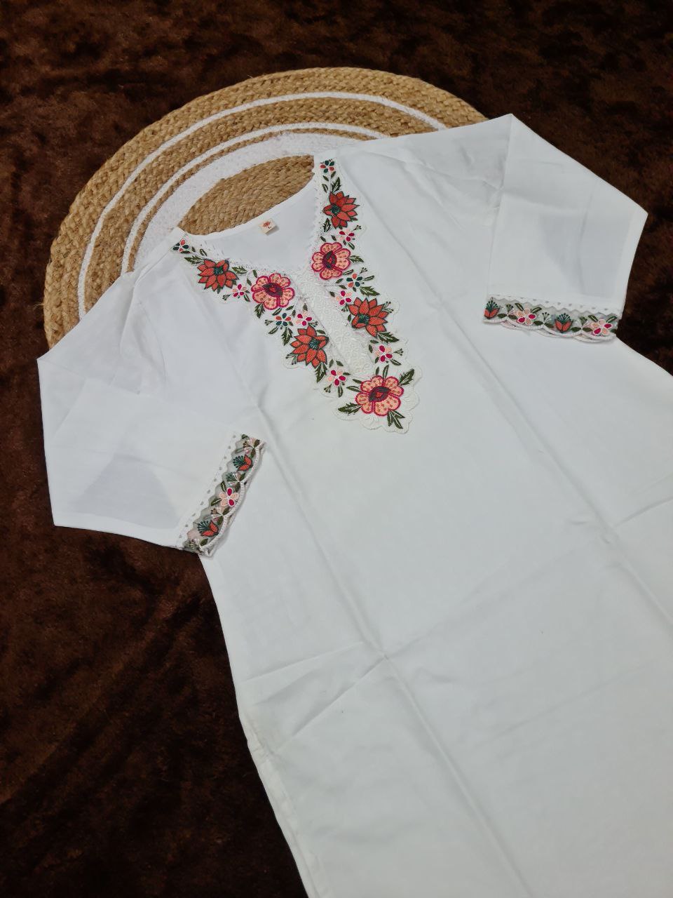 Detailed flat lay of the TRENDBUY white embroidered kurti, showcasing the sleeve embroidery and neckline, laid out on a brown textured surface.