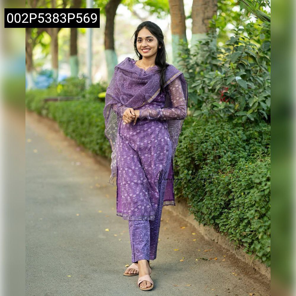 Smiling model wearing TRENDBUY purple Kota Chex kurti set with white botanical digital prints and sheer dupatta, walking outdoors.