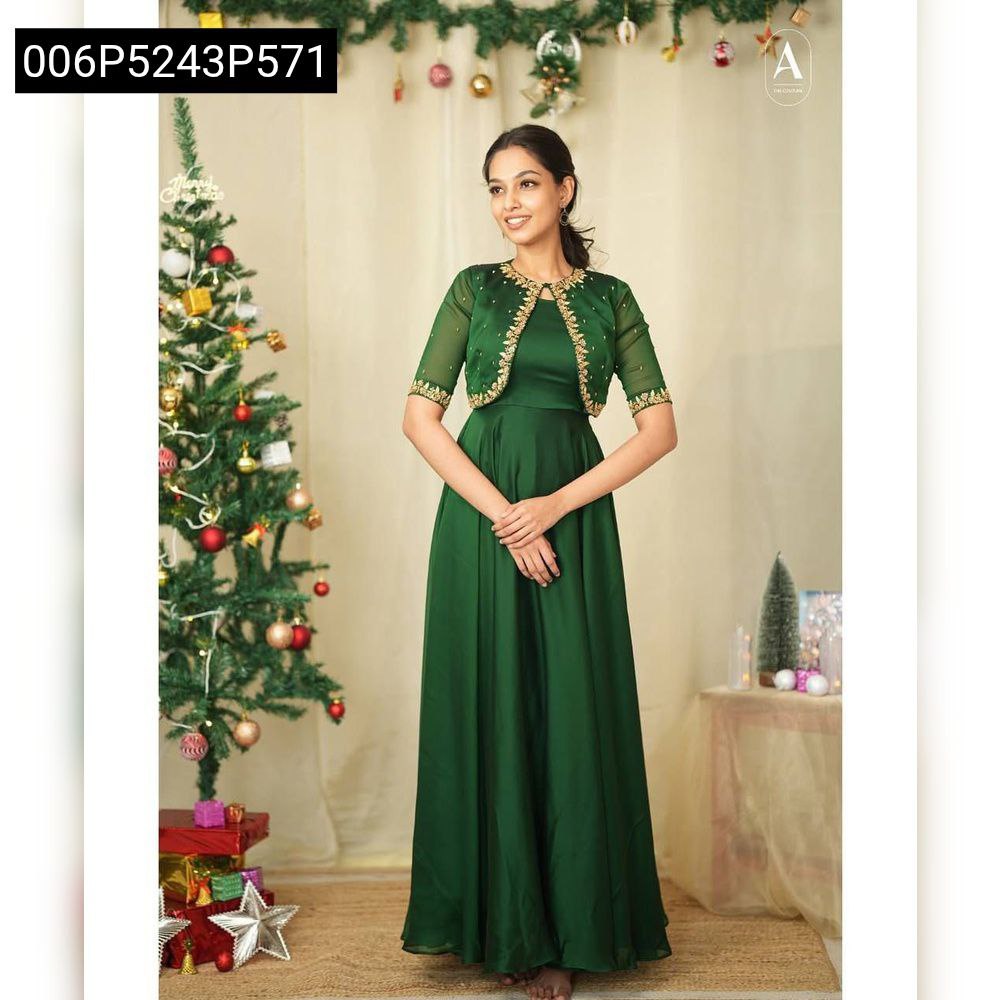Full body shot of a model elegantly posing in a green georgette gown with a golden embroidered shrug by a Christmas tree.