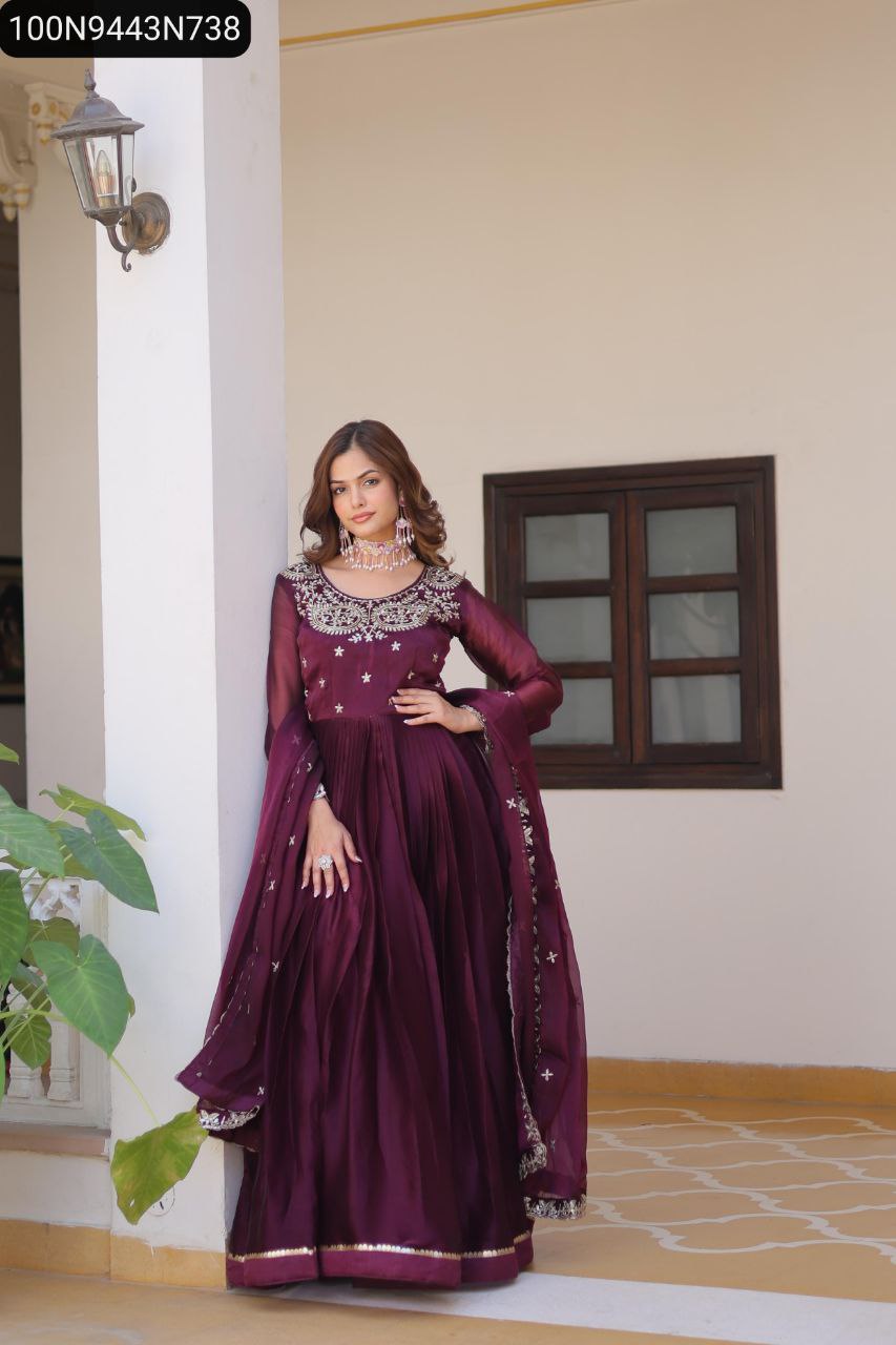 Full shot of a woman in a plum embroidered burberry silk anarkali gown, posing gracefully against a wall.