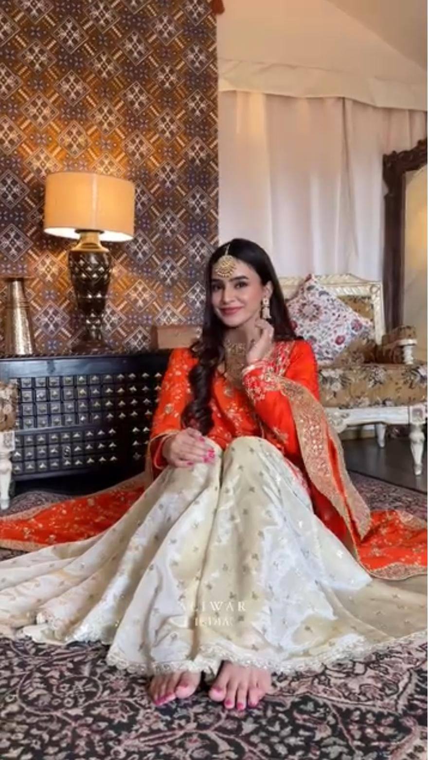 Woman posing in a beautiful orange and cream embroidered Chinon silk party wear top and palazzo set with dupatta and traditional jewelry.