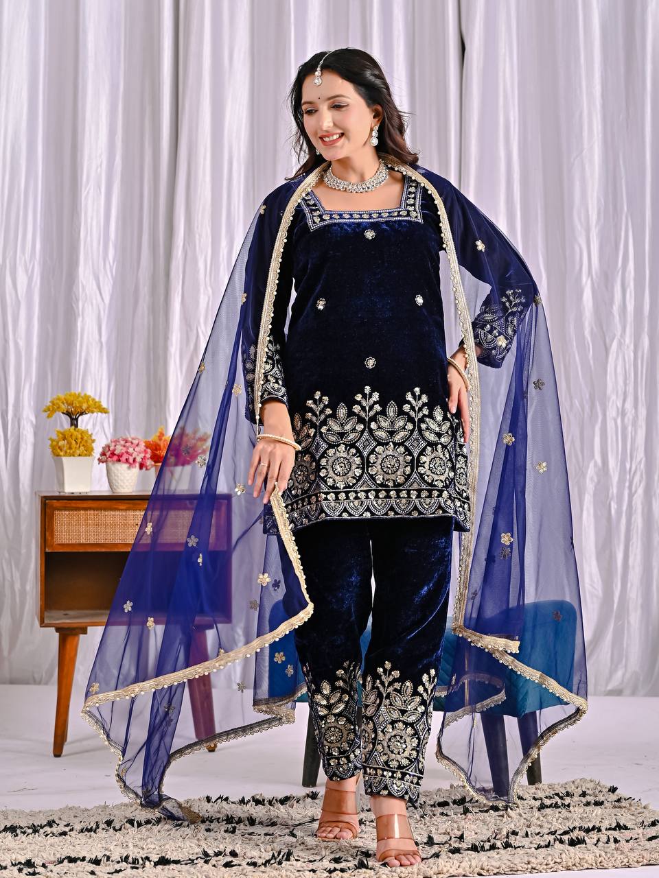 Full-body front view of a woman showcasing a luxurious navy blue velvet suit, richly embroidered with floral and geometric patterns, ideal for festive occasions.