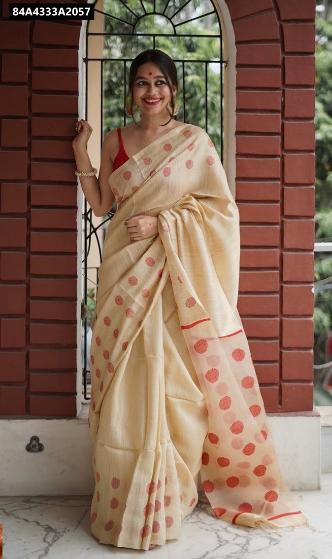 Full shot of a woman modelling a cream Lilan Slab saree with red polka dots, standing in an arched doorway, smiling at the camera.