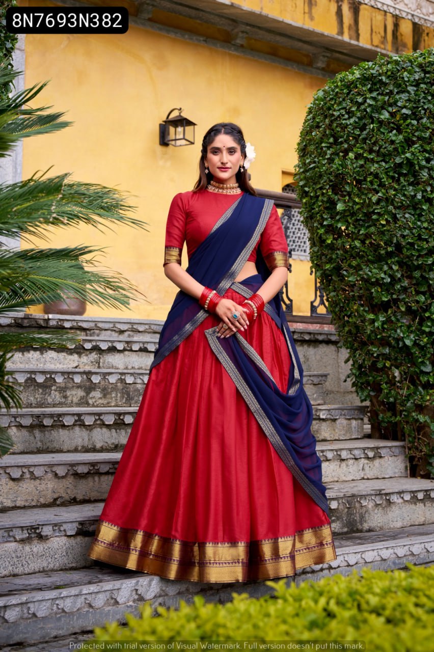 TRENDBUY model in a vibrant red lehenga choli with a navy blue dupatta, featuring intricate zari weaving, standing elegantly on stairs.