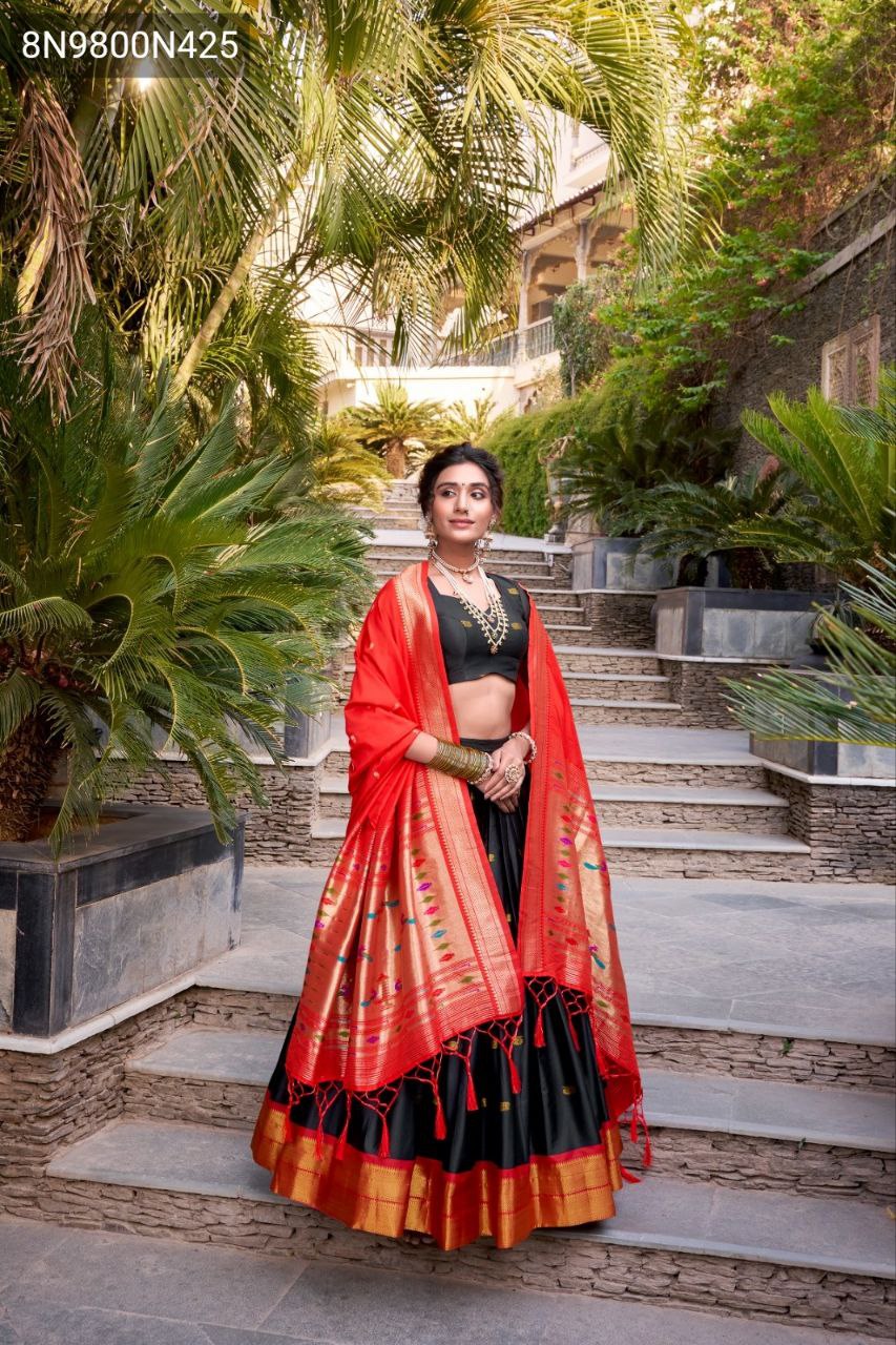 Model in black lehenga and red dupatta, standing full-length with hands folded, looking directly at the camera on stone steps, serving as the main product image.