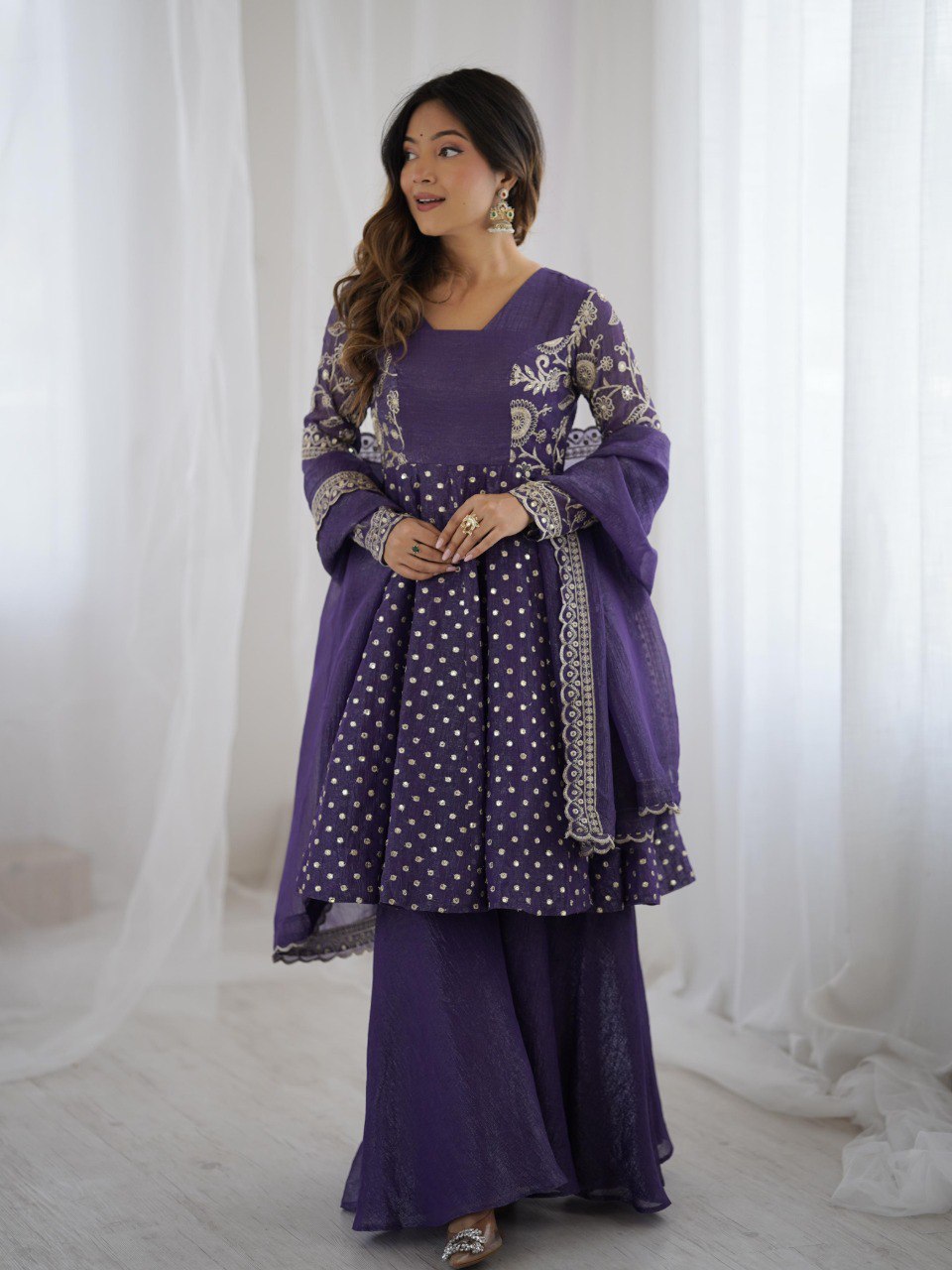 Woman in a purple embroidered silk sharara suit, facing left, showing off the full outfit.