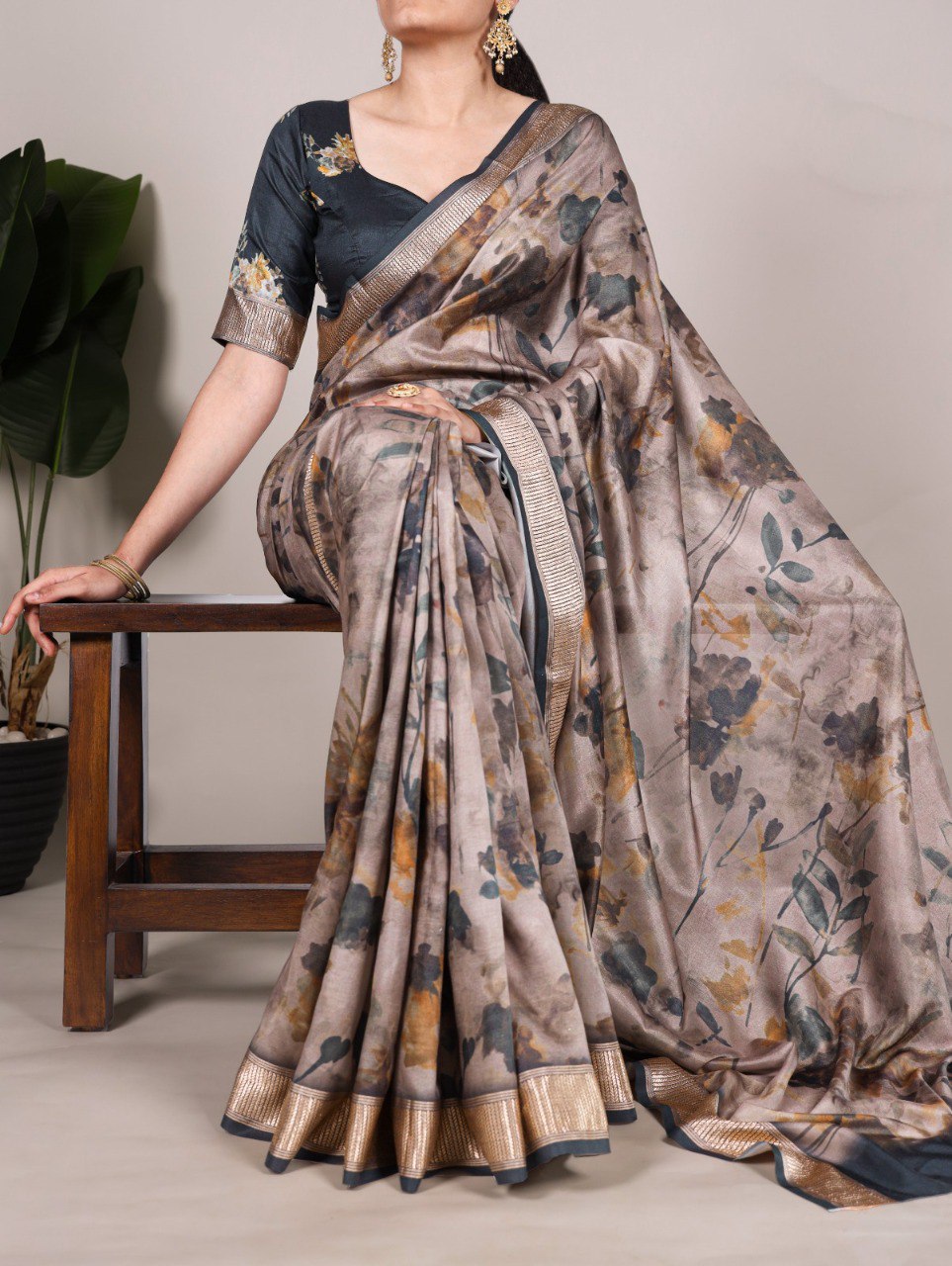 Woman wearing a beige Tussar silk printed saree with a dark grey blouse, sitting on a wooden stool.