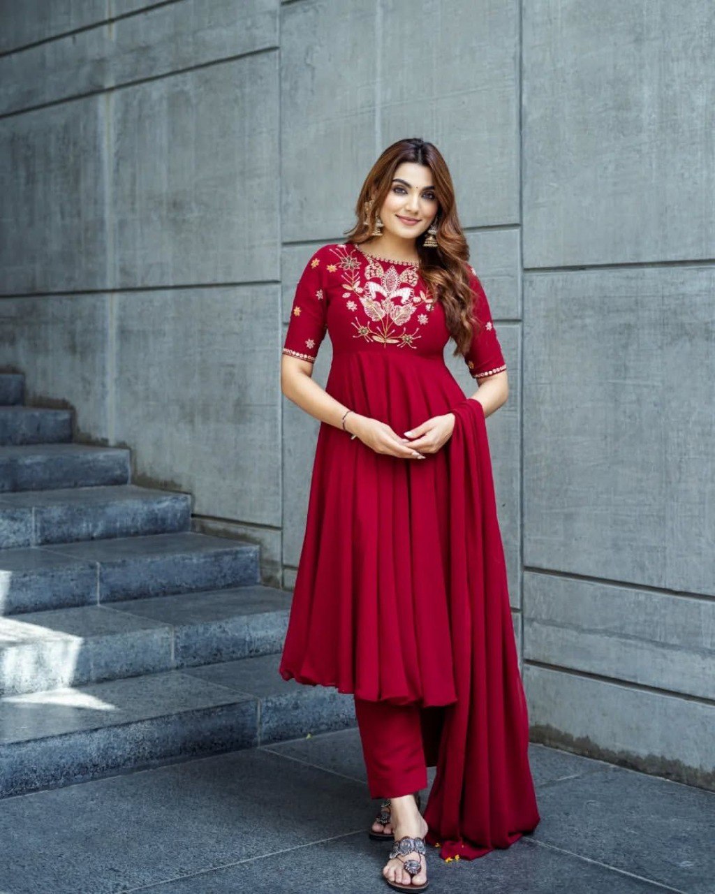 Model wearing a red designer Anarkali suit with intricate embroidery and a matching dupatta.