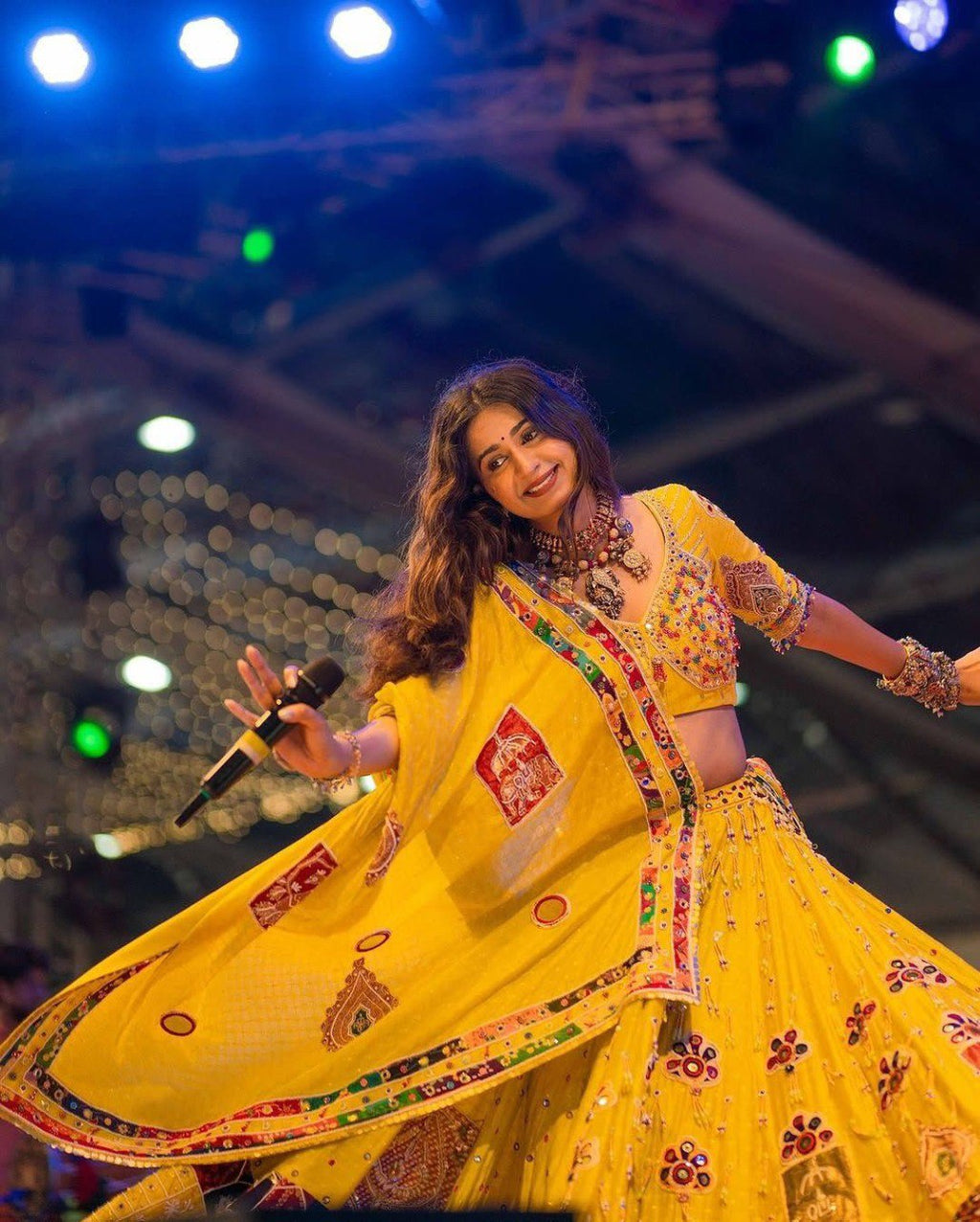 Model wearing a vibrant yellow Navratri Chaniya Choli with intricate mirror work and embroidery, performing on stage.