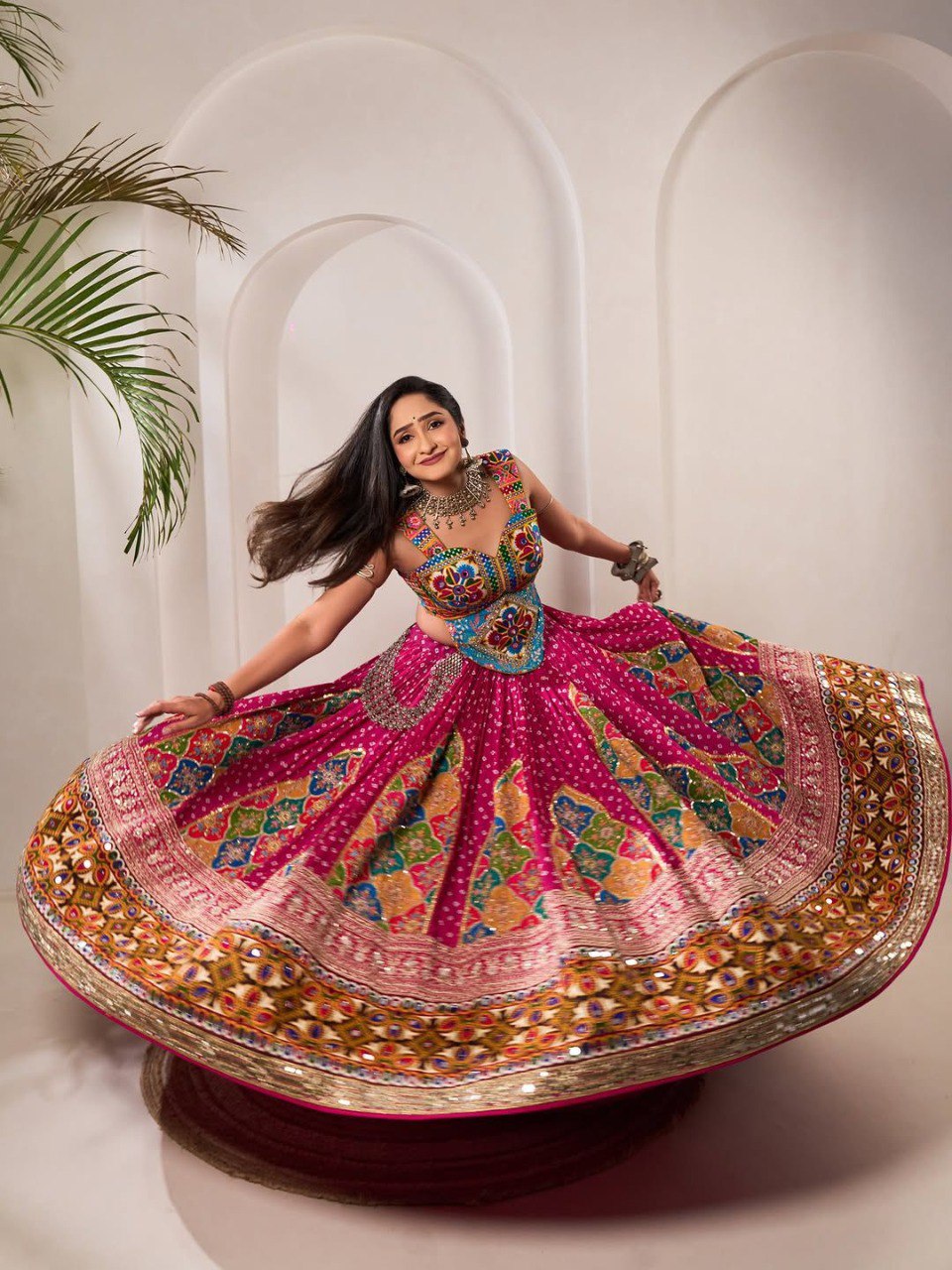 Woman twirling in a vibrant pink Navratri Chaniya Choli with intricate digital prints and mirror work.