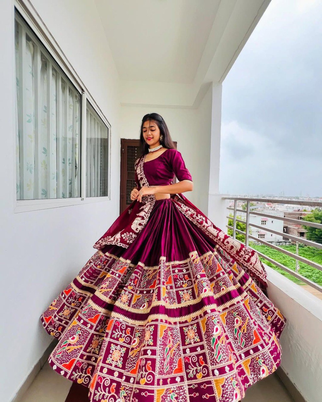 A smiling woman posing in a maroon Chaniya Choli, highlighting the beautifully embroidered border and mirror work on the lehenga.