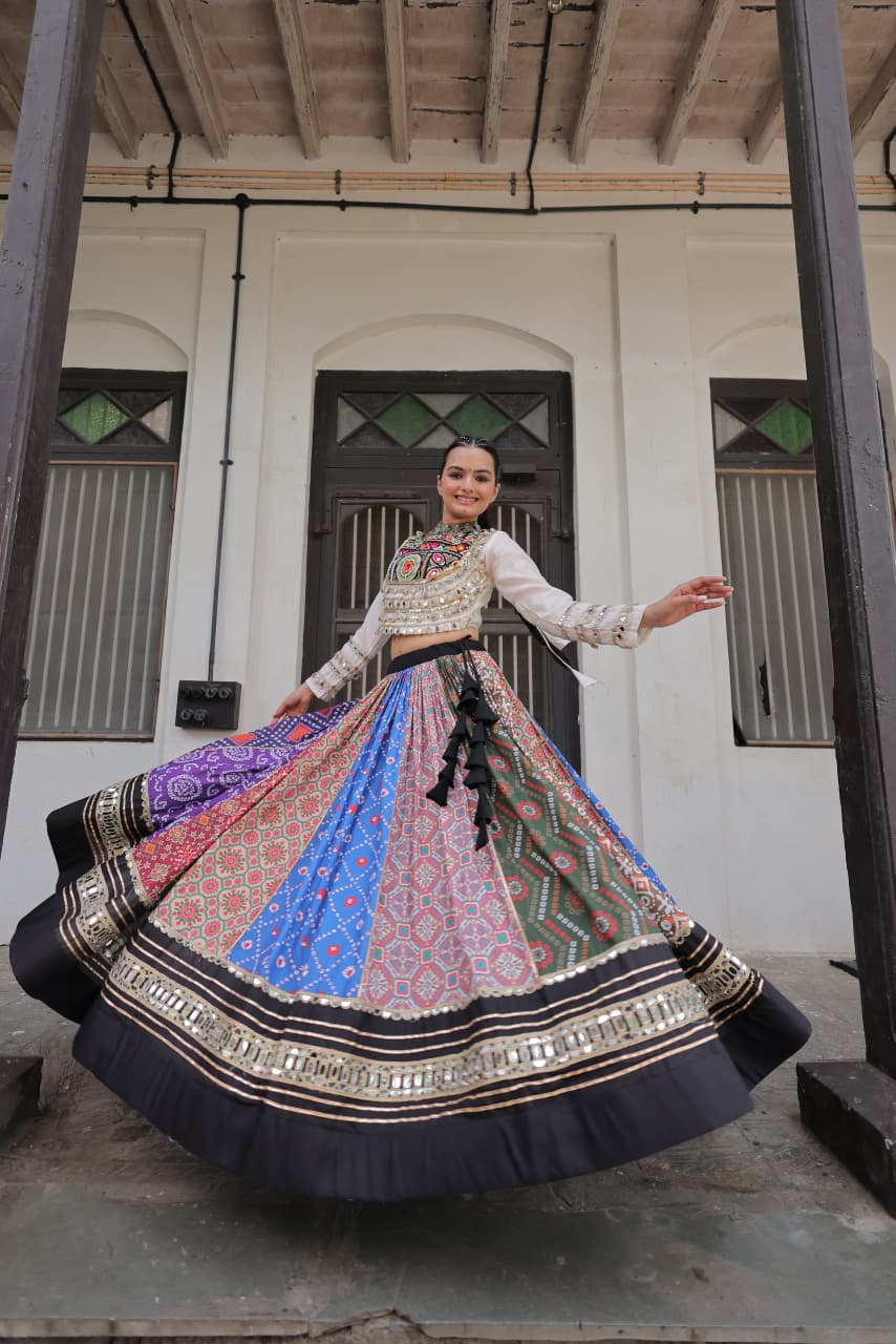 Model in vibrant multi-color Navratri lehenga choli with mirror work, twirling gracefully in front of a traditional building.
