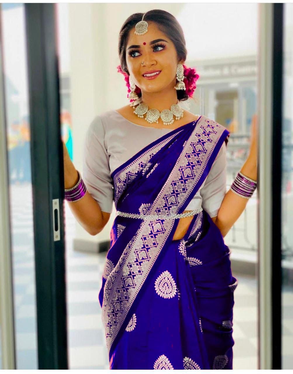 Model smiling, showcasing a vibrant royal blue Lichi Silk Saree with silver Jacquard weave and traditional jewelry.