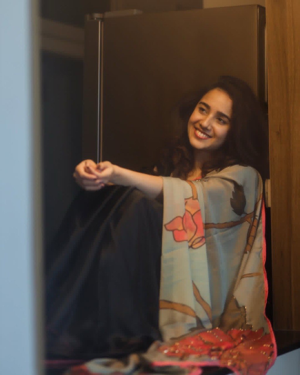 Young woman gracefully draped in the TRENDBUY half-half Japan satin saree with digital floral print, smiling gently while seated indoors.