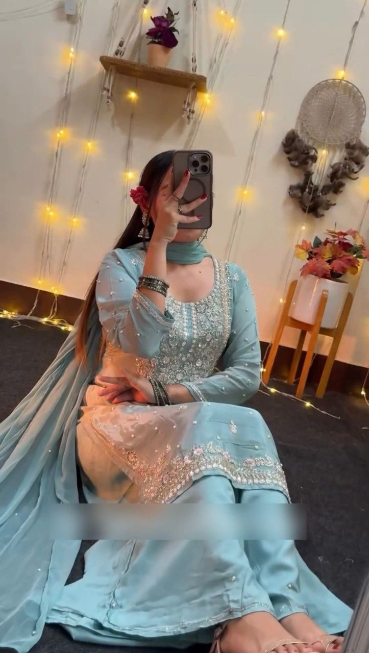 Woman showcasing the aqua blue faux georgette plazzo suit, posing gracefully in a mirror, highlighting the flow and fit, illuminated by fairy lights.