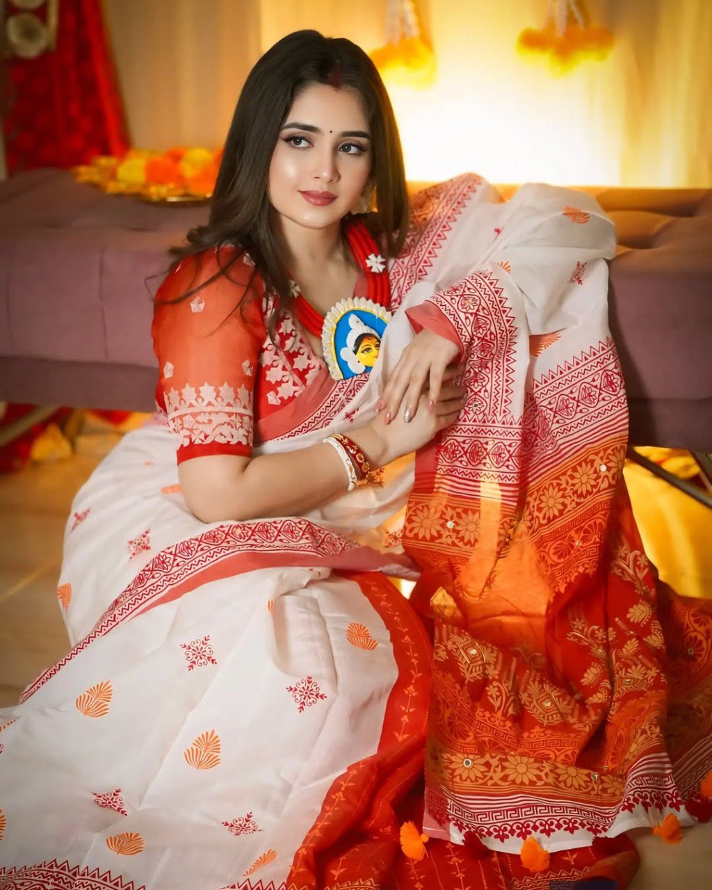 Model in white and red heavy linen saree with Durga Puja necklace, sitting gracefully for a festive photoshoot.