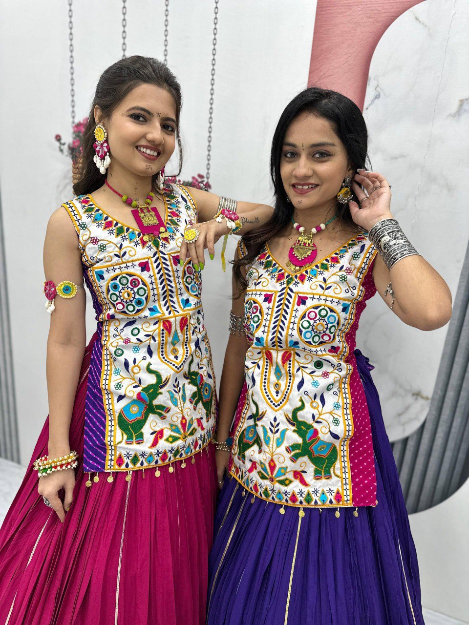 Two women in vibrant Navratri Lehenga Choli, one magenta, one purple, showcasing Gamathi and real mirror work