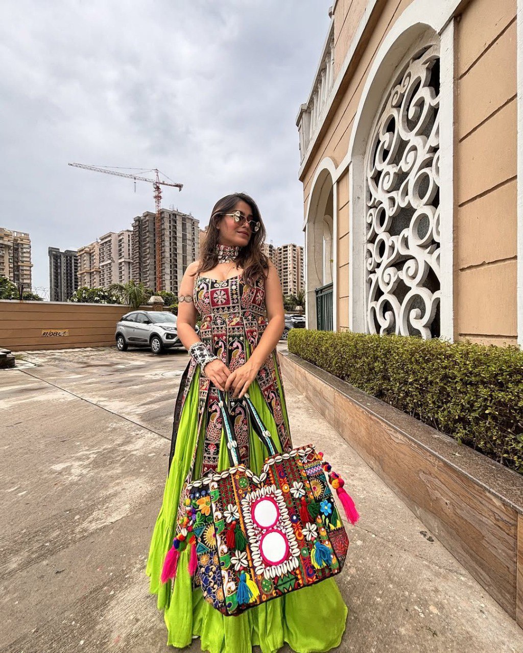 Woman in TRENDBUY Navaratri Georgette Lehenga Choli with sequence embroidery and a colorful embroidered bag, posing outdoors.