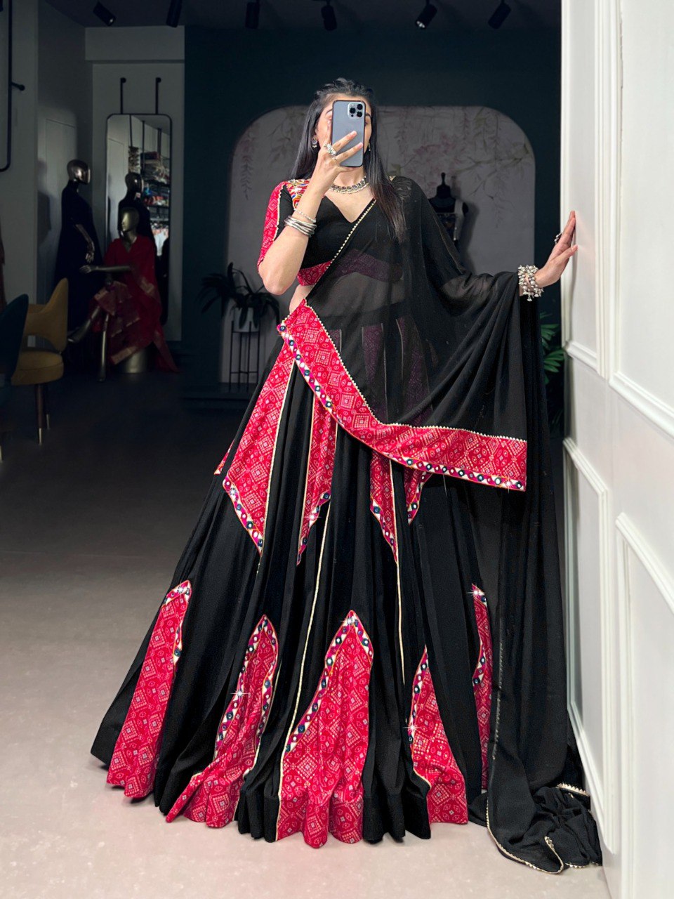TRENDBUY model showcasing a black and red Bandhej lehenga choli with mirror work, posing elegantly in a boutique.