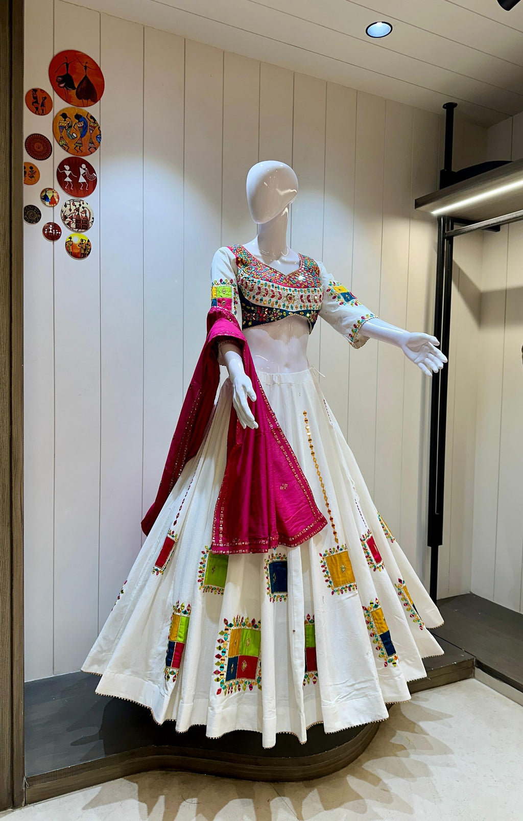 White Navratri chaniya choli set on mannequin with colorful traditional square patches and pink dupatta.