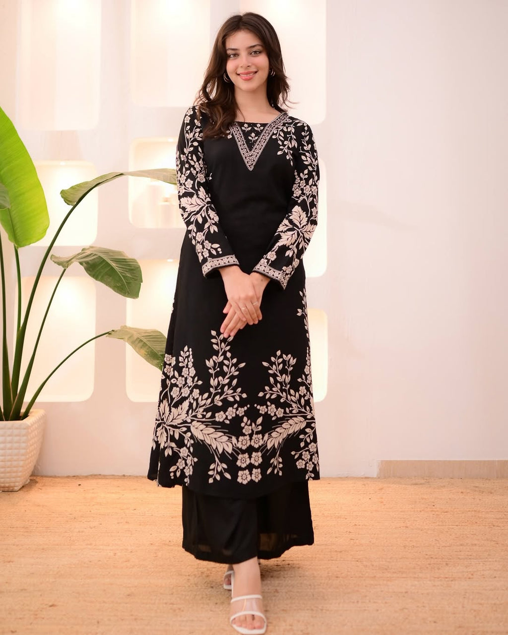 TRENDBUY model showcasing a black rayon slub 2-piece suit set with intricate white floral handwork embroidery, standing confidently against a warm background.