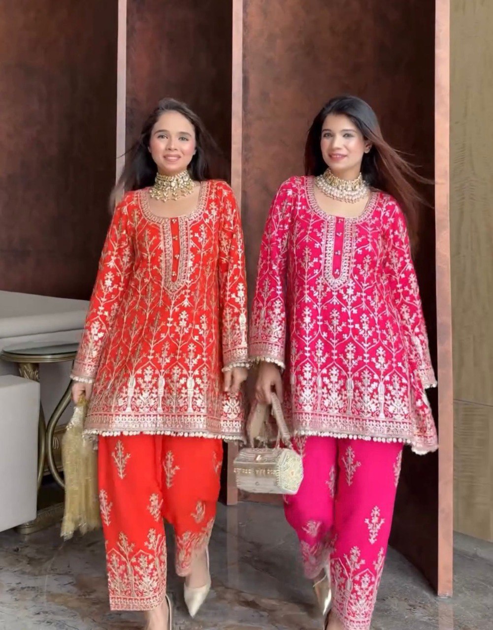 Two women in vibrant red/orange and hot pink embroidered faux georgette plazzo suits.