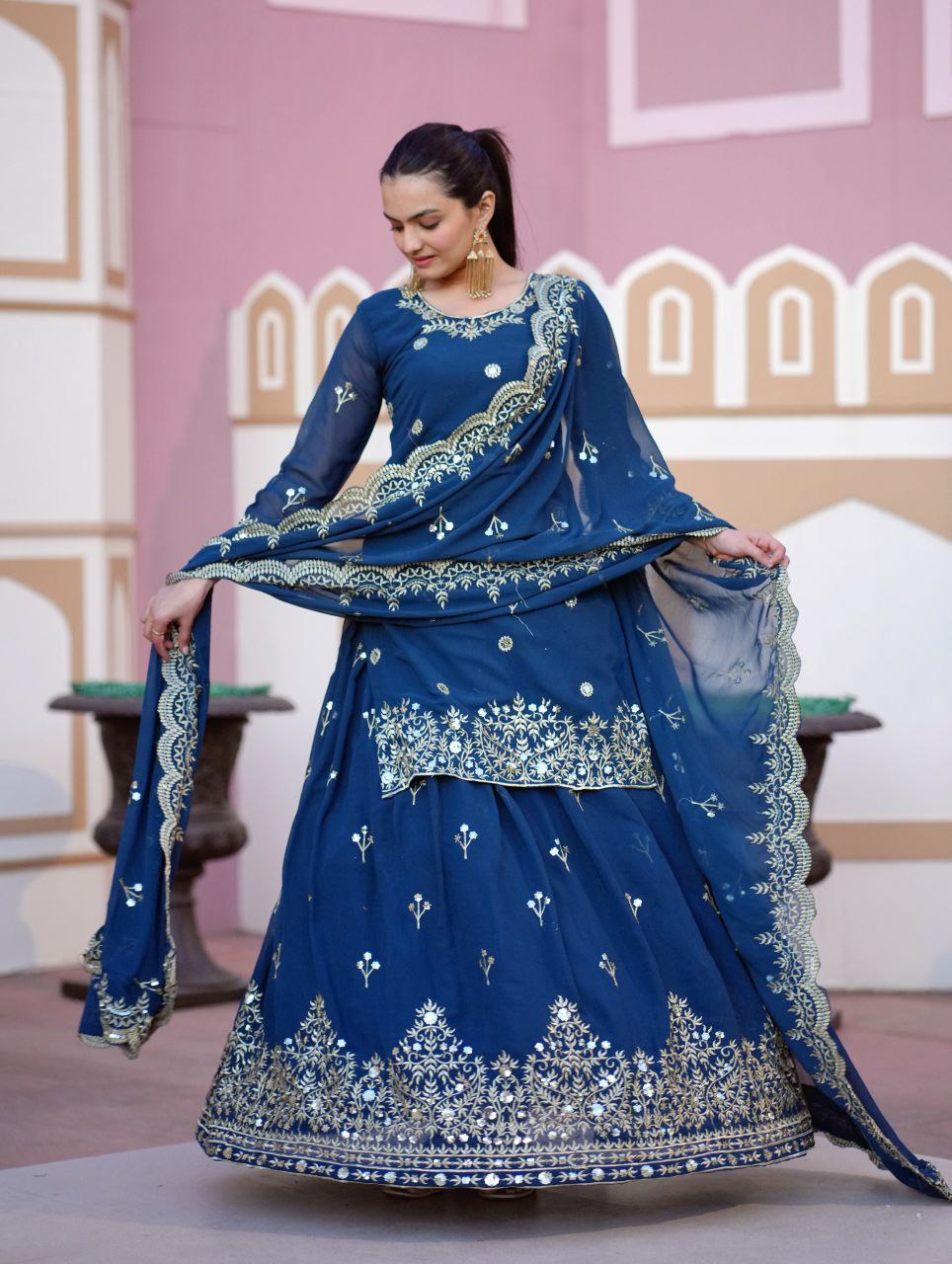 Model wearing a royal blue designer embroidered georgette lehenga suit with intricate gold sequence work and a matching dupatta.