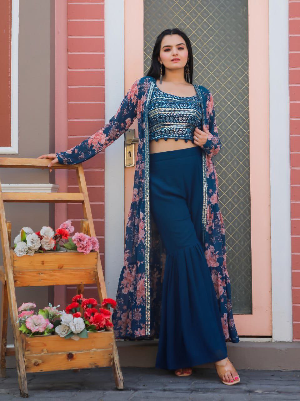 Model wearing a blue embroidered choli with a floral printed shrug and blue sharara pants.