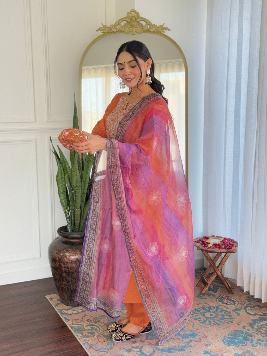 TRENDBUY woman in orange rayon embroidered kurta set holding a decorative bowl, elegant indoors.